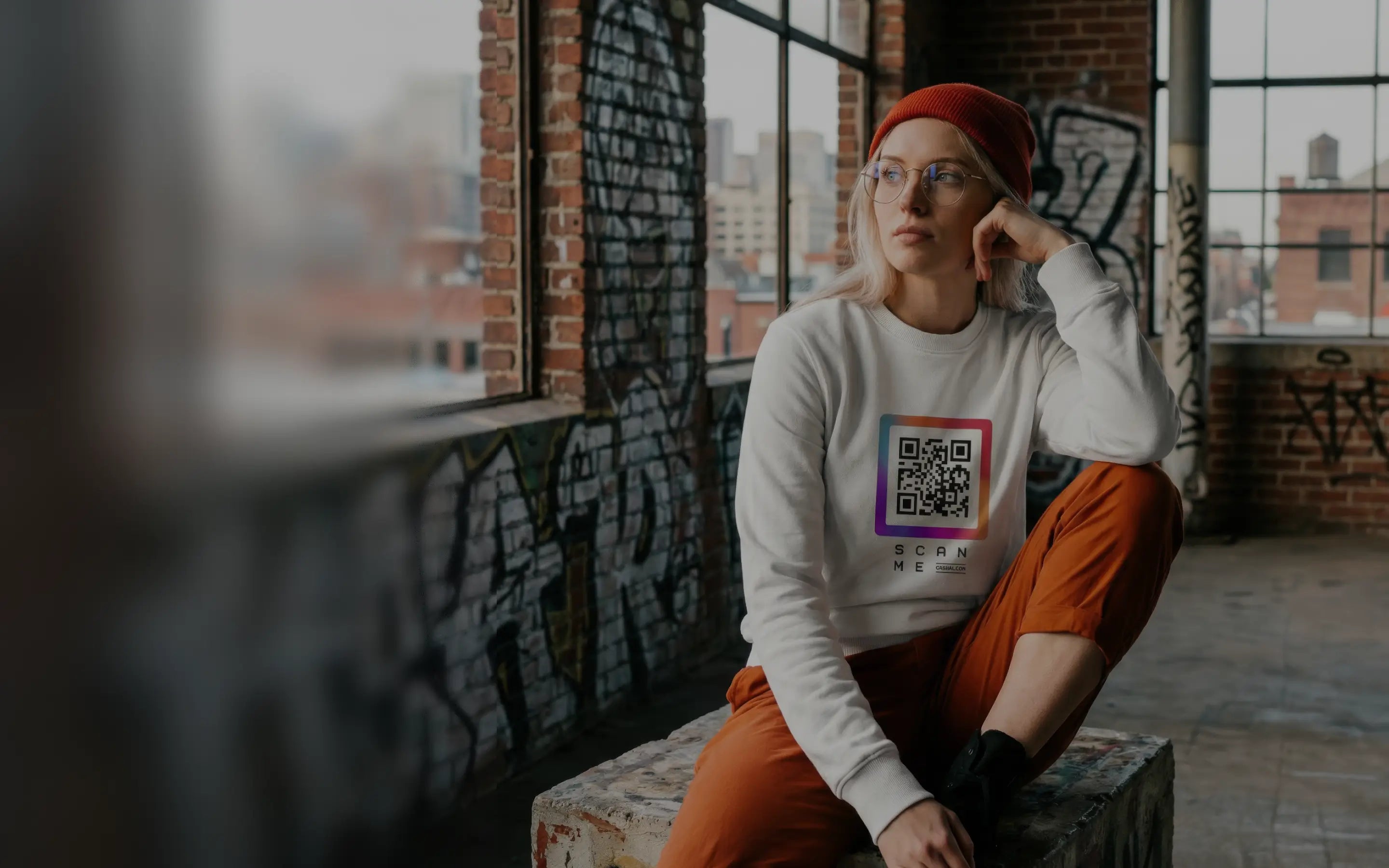 Woman in white sweatshirt with QR code, sitting in old building. Streetwear style.